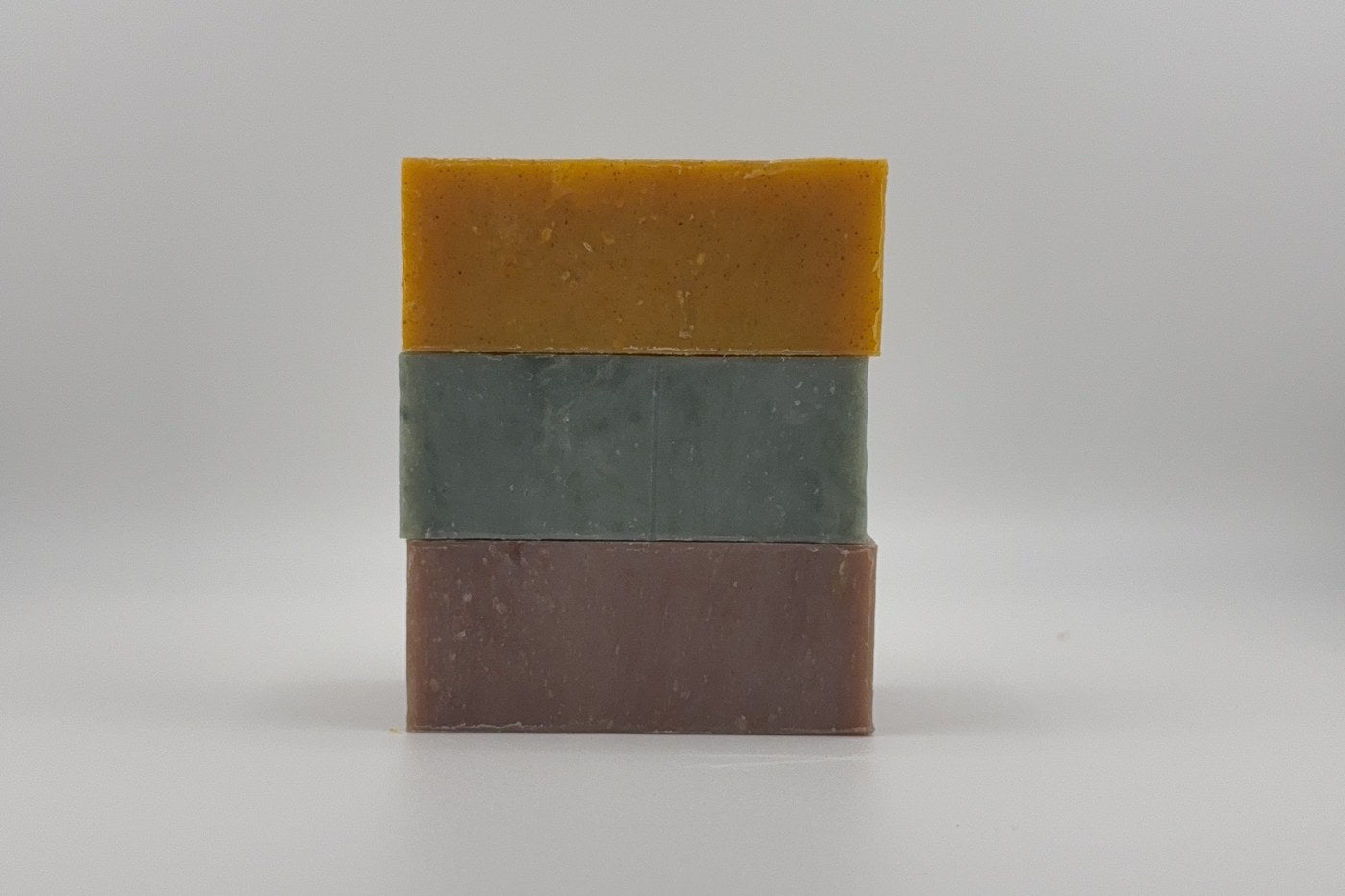 Three Kettner soap bars stacked: golden Bay Rum, green Pine Ridge and brown Bourbon Woods